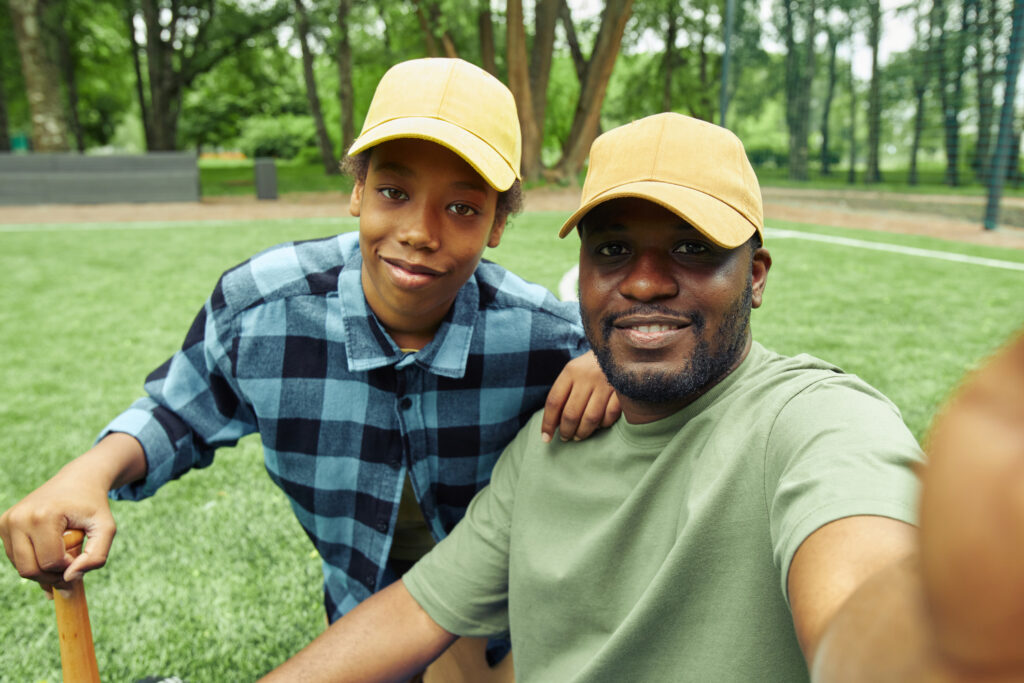A father and son in yellow caps taking a selfie in a park