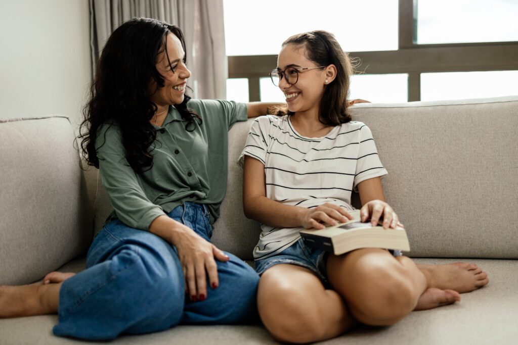 A mother and her teenage daughter sitting together and smiling.