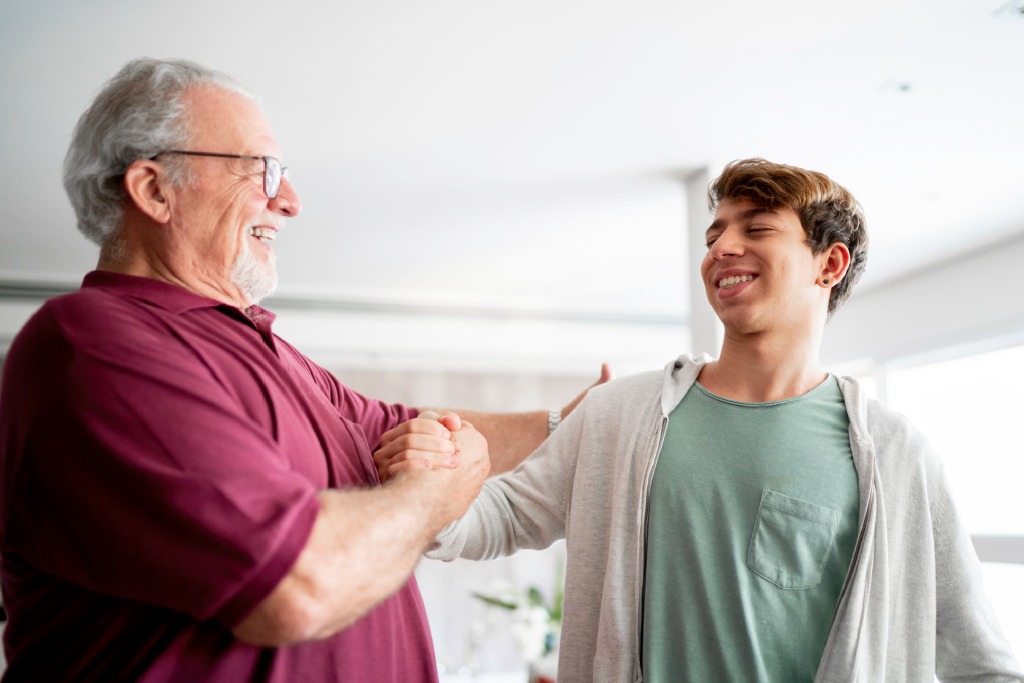 A teen and older man smile and embrace in a living room.