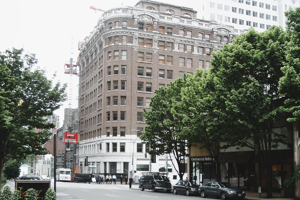 A Seattle street corner with a building, parked cars, and pedestrians.