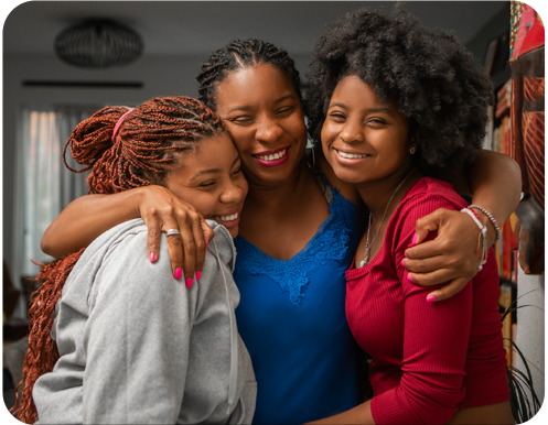A smiling woman hugs two smiling teens in a living room.