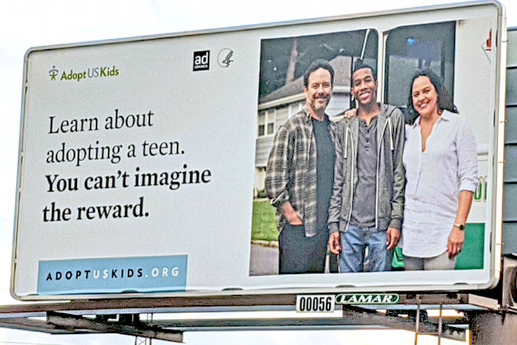 An AdoptUSKids billboard with image of family of two adults and one teen with the text "Learn about adopting a teen. You can't imagine the reward."