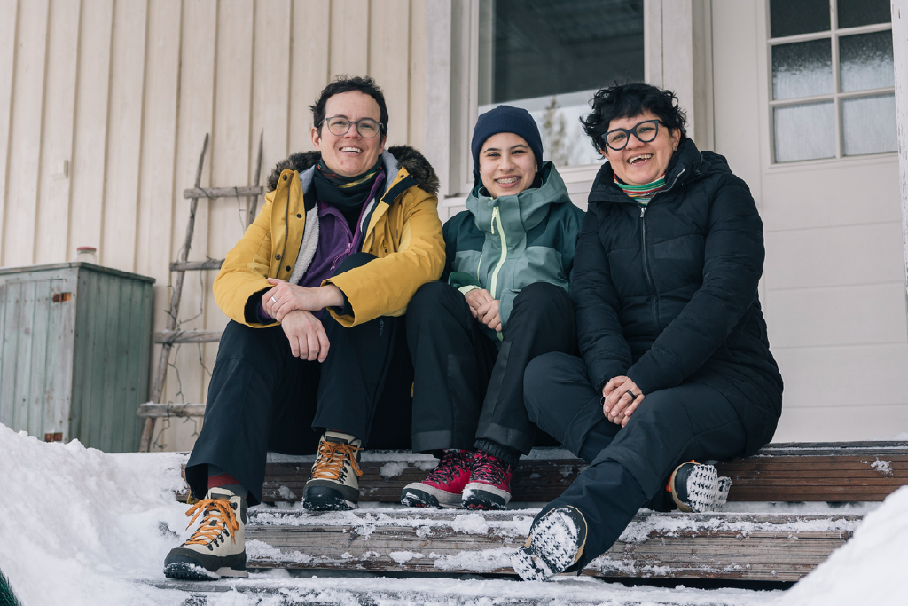 Two adults and a young person smiling together on a snowy porch.