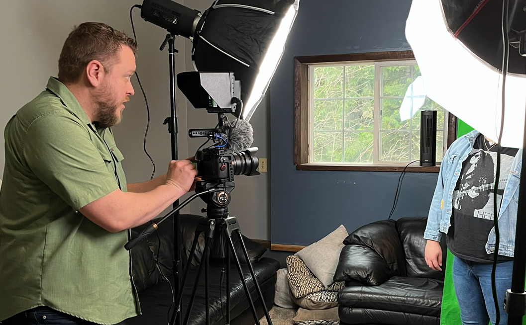 A youth engagement specialist works with a young person and camera equipment to create a profile in a living room studio.